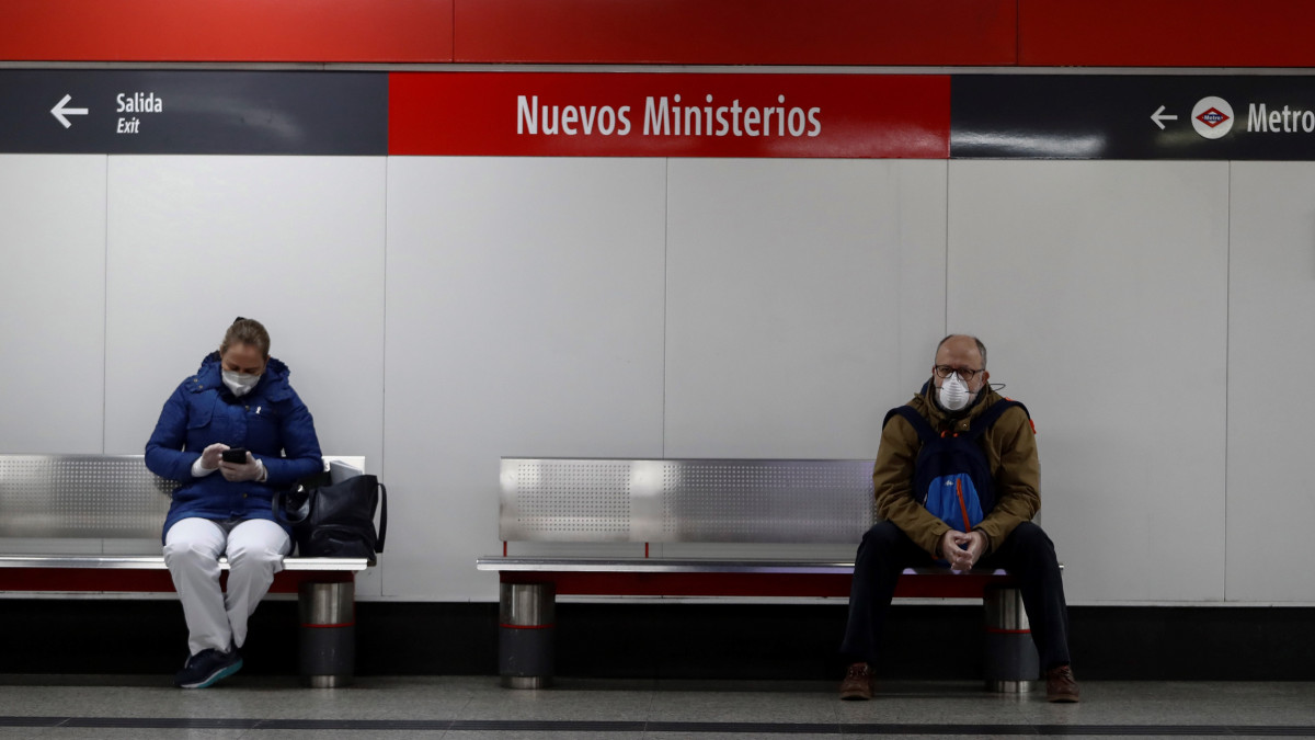 A koronavírus-járvány terjedése miatt védőmaszkot viselő utasok várják a vonatot a Nuevos Ministerios vasútállomáson Madridban 2020. március 19-én. Spanyolország öt nappal ezelőtt kijárási korlátozást vezetett be. Az országban eddig 14769 fertőzött személyt regisztráltak és 638 ember vesztette életét.