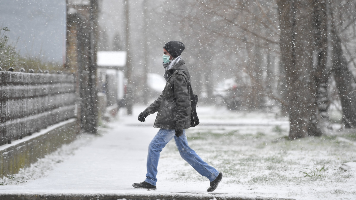 A koronavírus-járvány miatt szájmaszkot viselő férfi hóesésben Debrecenben 2020. március 23-án.