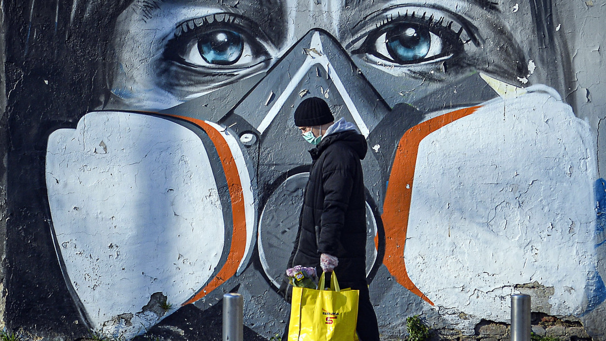 Védőmaszkos embert ábrázoló falfestmény előtt egy járókelő Milánóban 2020. március 16-án, amikor a tüdőgyulladást okozó koronavírus terjedésének megfékezésére vesztegzár van érvényben egész Olaszországban.