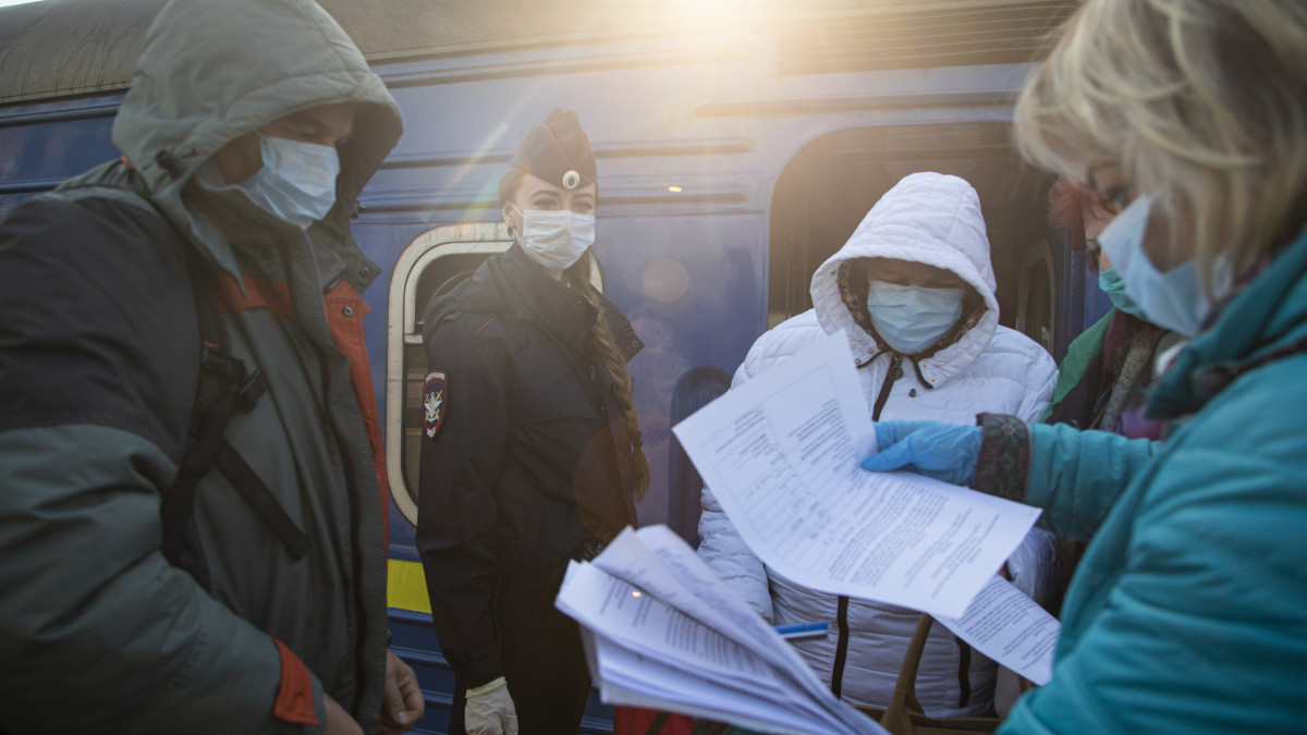 Védőruházatot viselő munkások ellenőrzik a Kijevből érkező utasok iratait a moszkvai Kijevszkij vasútállomáson 2020. március 28-án. Az orosz állami vasúti társaság különvonatot indított az orosz állampolgárok Ukrajnából és az ukránok Oroszországból történő hazaszállítására, miután az ukrán kormány bejelentette, hogy a koronavírus-járvány miatt Ukrajna teljesen leállítja a nemzetközi utasszállítást, azaz lezárja határait saját állampolgárai előtt is.