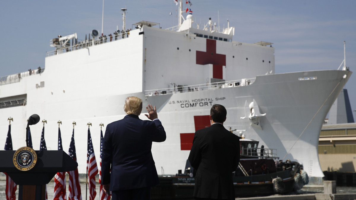 Donald Trump amerikai elnök (b) és Mark Esper védelmi miniszter nézi, ahogy a haditengerészet Comfort nevű kórházhajója elhagyja Norfolk kikötőjét 2020. március 28-án. A hajó New Yorkba tart, hogy ott segítse a koronavírus elleni küzdelmet. Az Egyesült Államokban 113 ezer fölé emelkedett a fertőzöttek száma, a járványban eddig 1902-en vesztették életüket.
