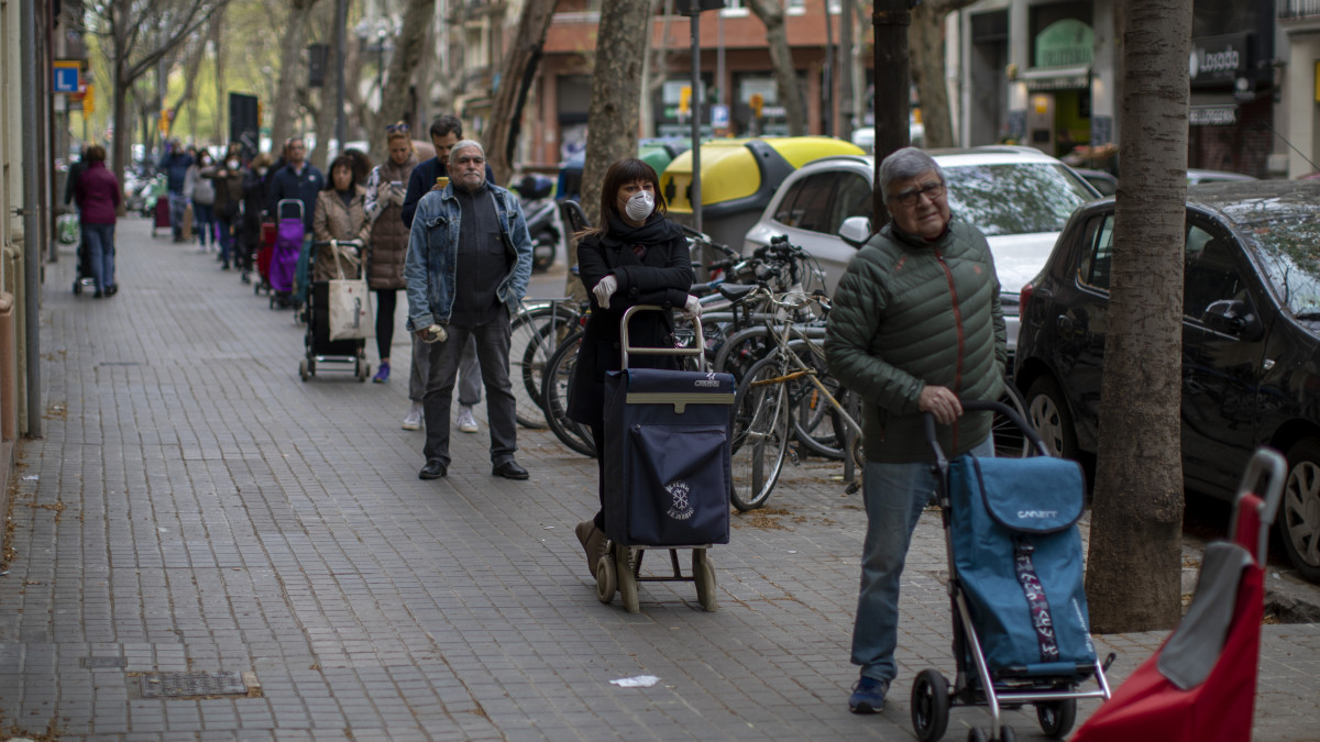 Biztonságos távolságra sorakoznak egymástól a vásárlók egy barcelonai üzlet előtt 2020. március 27-én. Spanyolországban 57 786-ra emelkedett a fertőzöttek száma, a járványban eddig 4365-en vesztették életüket.