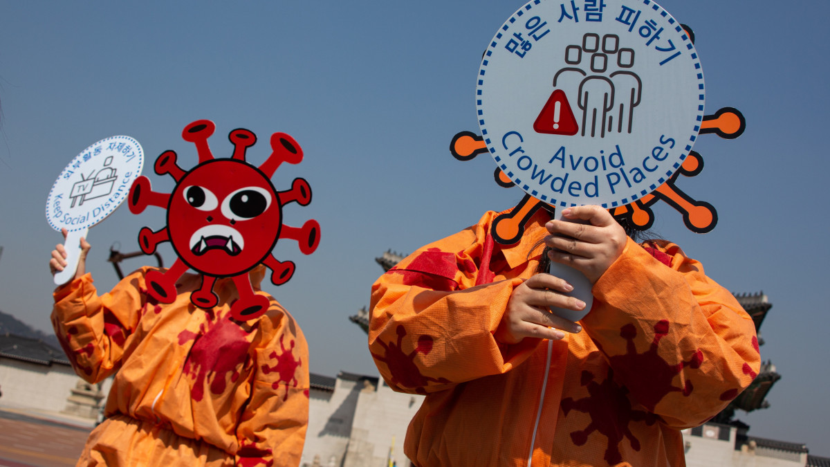 Dél-koreai környezetvédők a koronavírus tüskéit formázó maszkban hívják fel a figyelmet a koronavírus-járvány idejént elvárt higiénés óvintézkedések kötelező és rendszeres megtételére Szöul belvárosában 2020. március 30-án. A felirat szövege: Közösségi távolságtartás (b), Zsúfolt helyek kerülése.