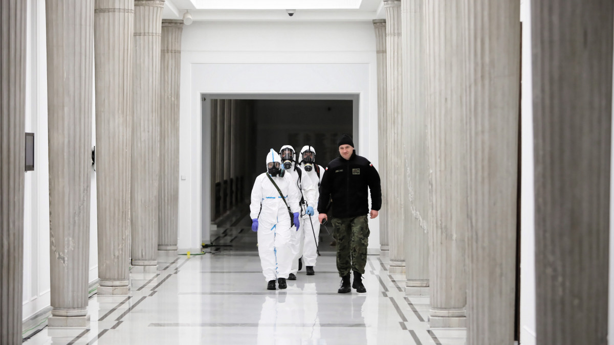 A koronavírus-járvány miatt védőruhát viselő egészségügyi alkalmazottak fertőtlenítést végeznek a lengyel parlamenti alsóháznak, a szejmnek otthont adó épületben, Varsóban 2020. március 31-én. 