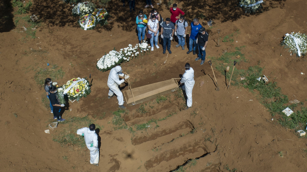 Védőruhát viselő temetői dolgozók a földbe engednek egy koporsót a brazíliai Sao Paulo város Vila Formosa temetőjében 2020. április 1-jén. A koronavírus-járvány miatt 30 százalékkal nőtt a temetkezések száma a brazil nagyvárosban.