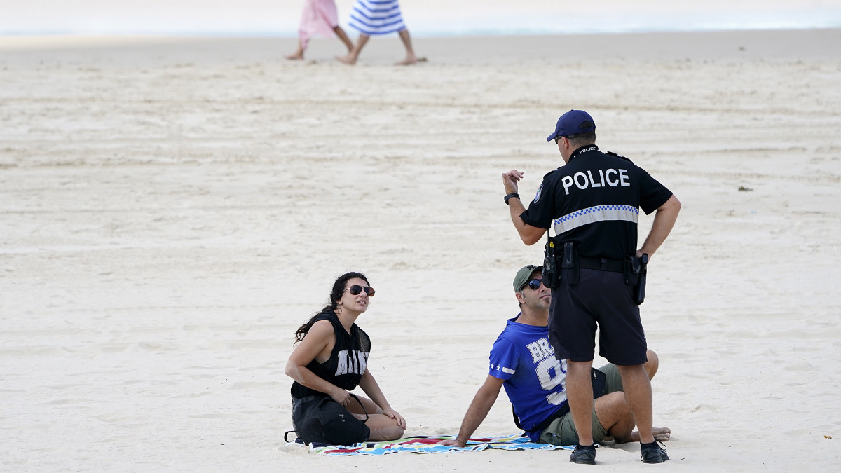 Rendőr beszél a napozó emberekkel az ausztráliai Queensland állam Gold Coast városának tengerpartján 2020. április 2-án. Az ausztrál szövetségi államban a koronavírus-járvány terjedésének megfékezésére bevezetett karanténszabályok megengedik a szabadidős sporttevékenység gyakorlását.