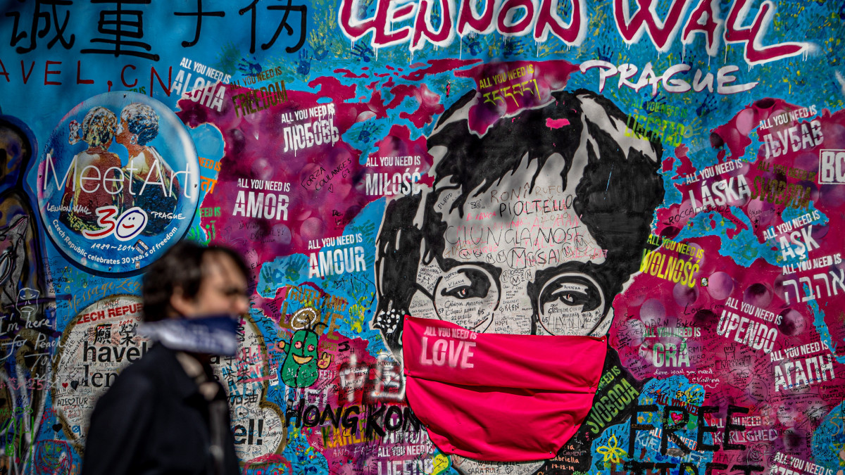 John Lennont, a The Beatles brit beatzenekar néhai énekesét védőmaszkban ábrázoló falfestmény előtt megy egy maszkot viselő férfi Prágában 2020. április 6-án. A cseh kormány kijárási korlátozást vezetett be a koronavírus elleni védekezésképpen.