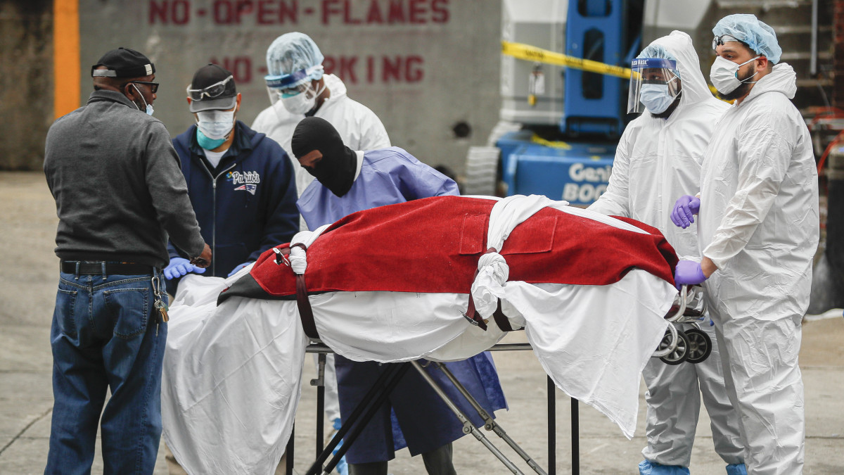 Egy átmeneti halottasházként működtetett hűtőkocsiból kiemelt holttestet halottaskocsihoz visznek a New York-i Brooklyn Kórházközpontnál 2020. március 31-én. Az új koronavírus okozta betegségben meghalt embert egy temetkezési vállalkozóhoz szállítják.
