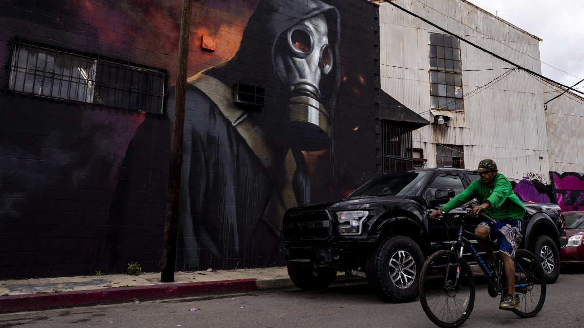 Biciklis halad el Rasmus Balstrom dán graffitiművész alkotása előtt Los Angelesben 2020. április 8-án, az egész világra kiterjedő koronavírus-járvány idején. A kép egy gázmaszkot viselő embert ábrázol.