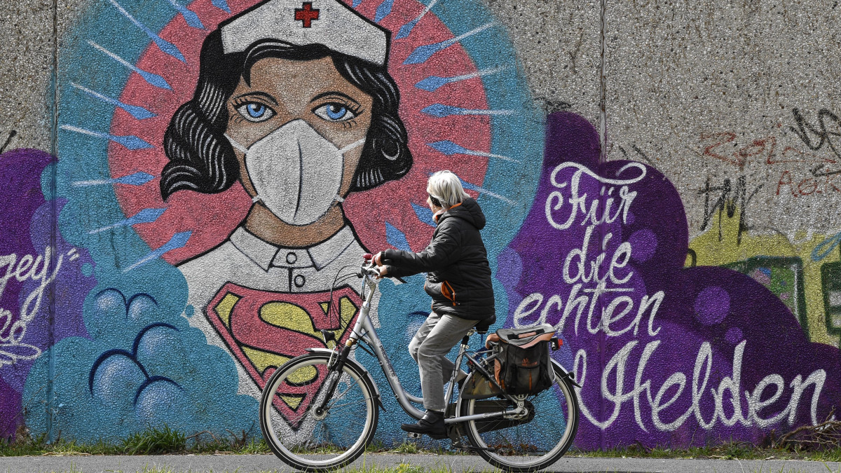 Kerékpáros halad el egy védőmaszkot viselő ápolónőt ábrázoló, az Uzey néven ismert utcaművész által készített graffiti előtt a koronavírus-járvány idején a németországi Hamm városában 2020. április 13-án. A kép melletti felirat jelentése: Az igazi hősöknek.
