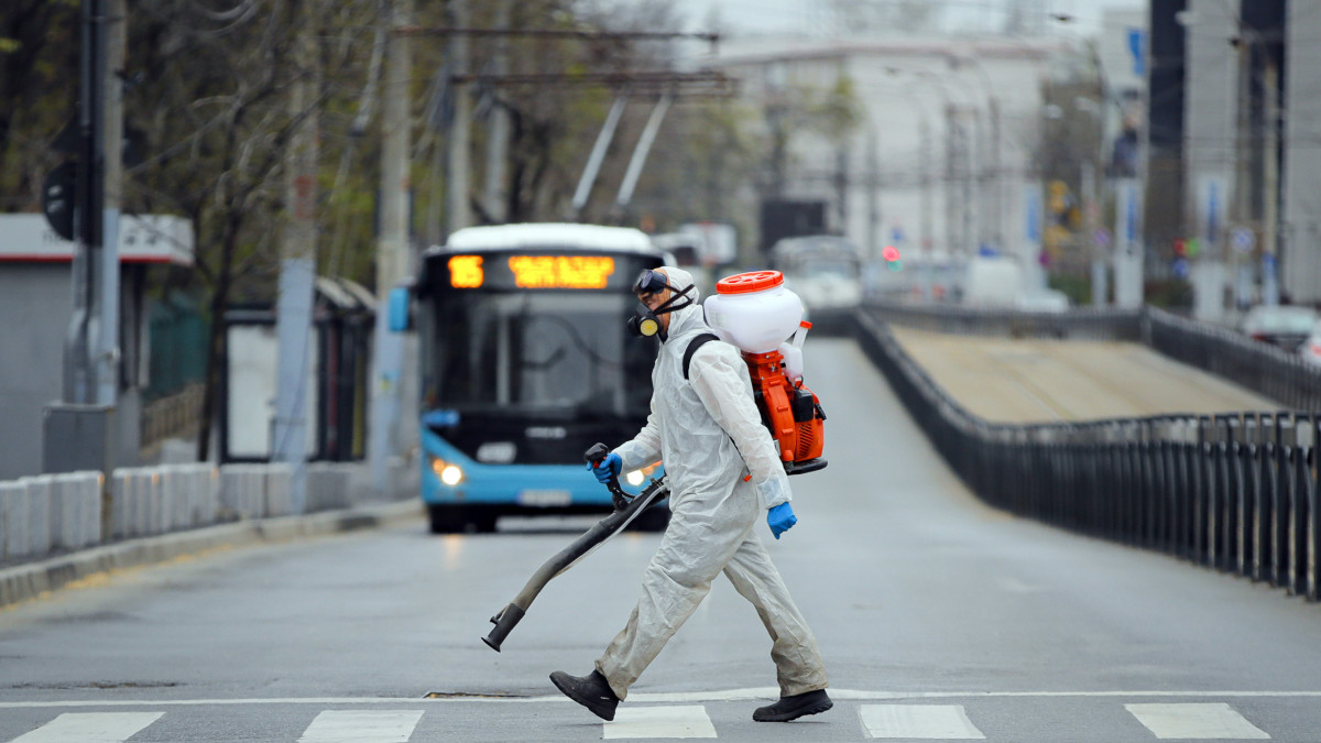 A koronavírus-járvány megfékezésének érdekében egy bukaresti utcát fertőtlenít védőruhás városi alkalmazott 2020. március 31-én.