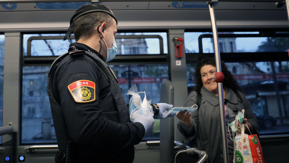 Védőmaszkot ad egy busz utasának egy rendőr a spanyolországi Valenciában a koronavírus-járvány idején, 2020. április 14-én, miután a spanyol kormány bizonyos, nem létfontosságú munkaterületek dolgozóinak feloldotta a kijárási korlátozást.