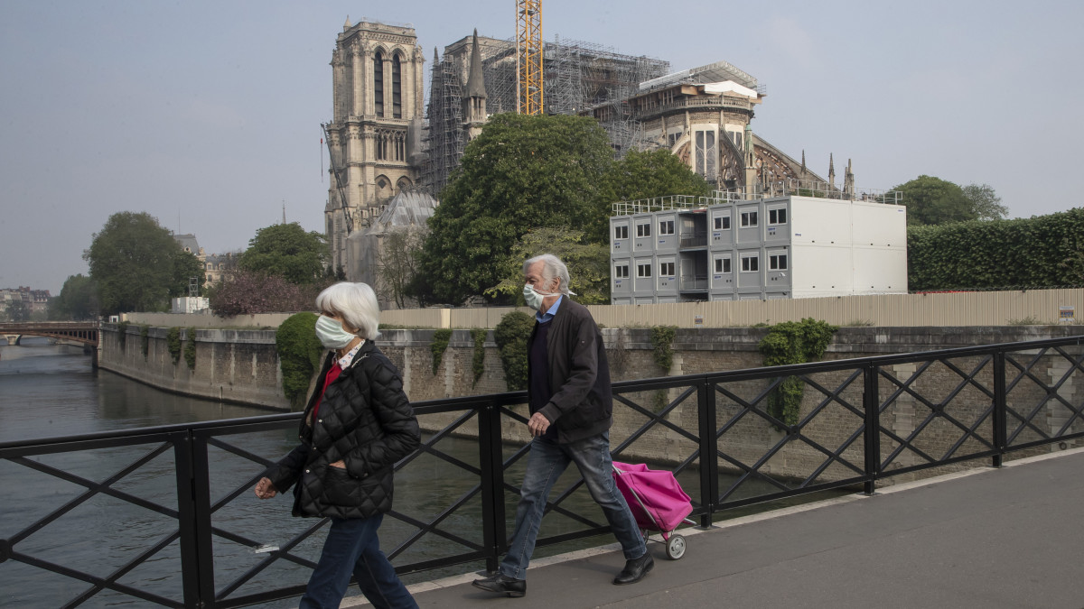 Védőmaszkot viselő emberek mennek át egy hídon a párizsi Notre Dame székesegyház közelében 2020. április 13-án. A gótikus katedrális huszártornya és gerendázata 2019. április 15-én megsemmisült egy tűzvészben. A folyamatban lévő felújítási munkálatokat a koronavírus-járvány miatt felfüggesztették.