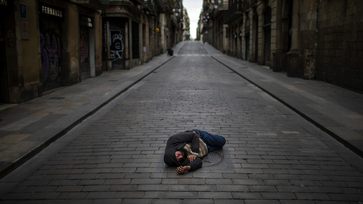 Hajléktalan férfi fekszik egy út közepén Barcelonában 2020. április 17-én, a koronavírus-járvány idején.