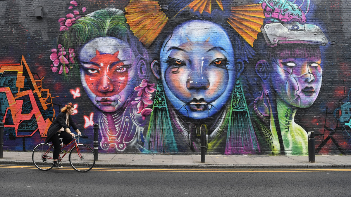 Kerékpáros egy falfestmény előtt az utcai művészek által kedvelt, máskor turistákkal teli kelet-londoni Brick Lane-en 2020. április 19-én, koronavírus-járvány idején.