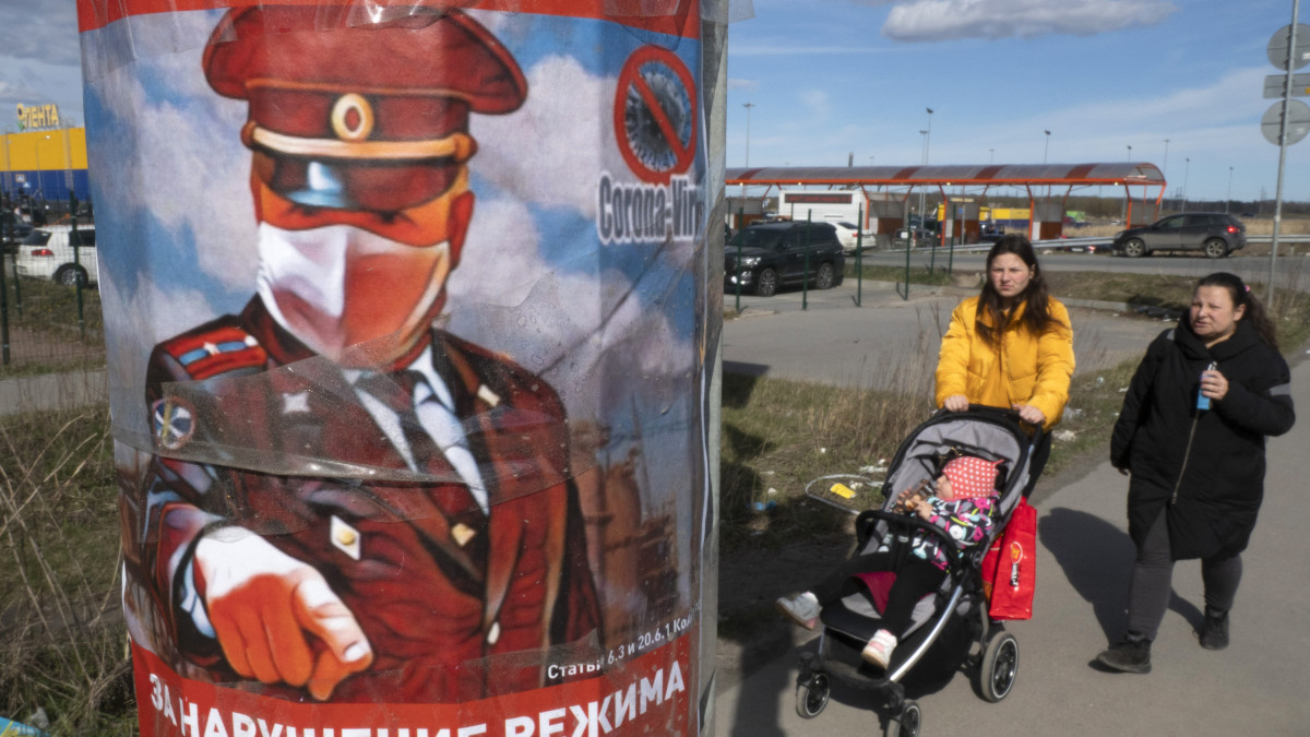Két nő halad el egy plakátoszlop mellett, amin egy rendőr felhívja a figyelmet a hatóságok által elrendelt kijárási korlátozások betartására Szentpéterváron 2020. április 21-én.