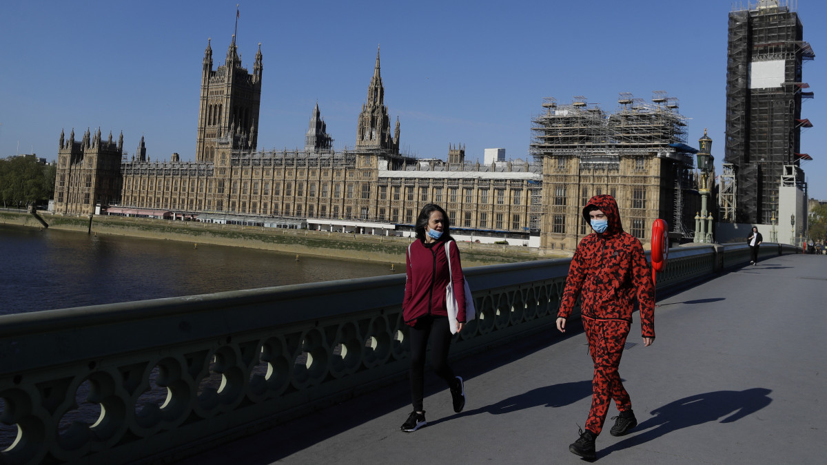 A londoni Westminster hídon, a parlament előtt mennek járókelők a koronavírus-járvány idején, 2020. április 21-én, amikor újra ülésezik a törvényhozás. A fertőzésveszély miatt kijárási korlátozás van érvényben Nagy-Britanniában, ezért a törvényhozók és a parlamenti dolgozók legnagyobb része is otthon tartózkodik, és a képviselők most is csak virtuálisan, az interneten keresztül összekapcsolódva ülnek össze.