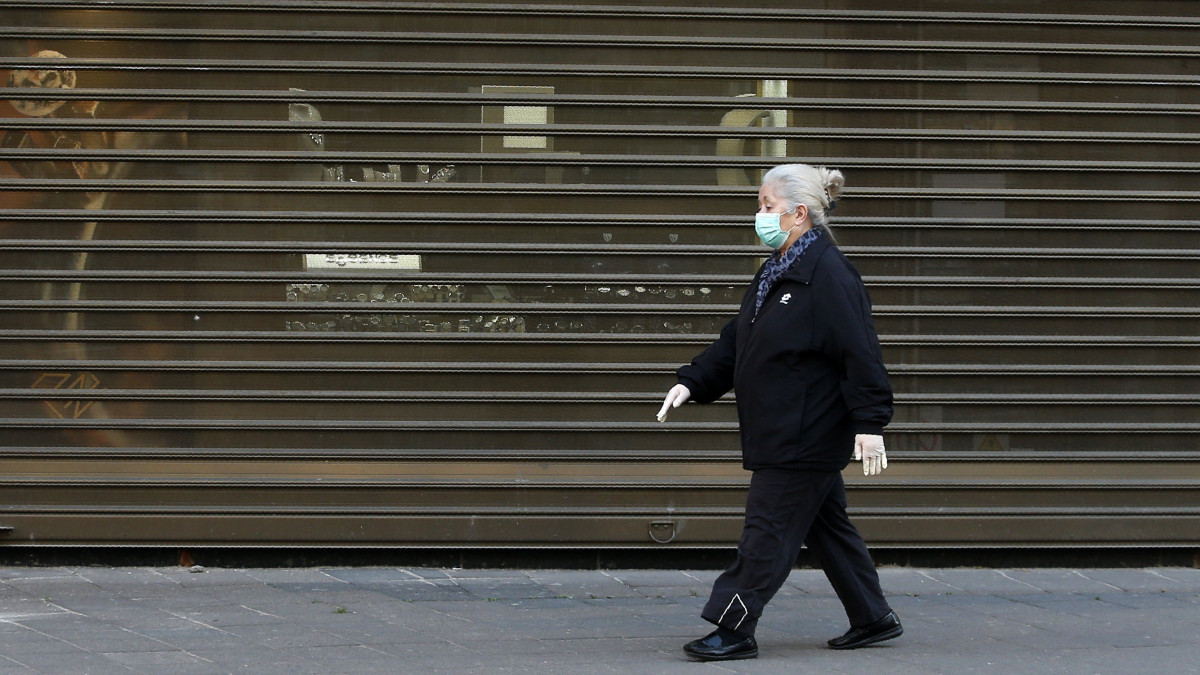 Védőmaszkot viselő idős nő megy egy belgrádi utcán 2020. április 21-én. Szerbiában ettől a naptól kezdve rövidítik a kijárási tilalom óráit, a március közepe óta szobafogságra ítélt nyugdíjasok heti háromszor rövid sétát tehetnek a lakhelyük környékén, és fokozatosan kinyithatnak a műhelyek, edzőtermek, fodrász- és kozmetikai szalonok, május közepétől pedig a szállodák és a vendéglátóhelyek is.