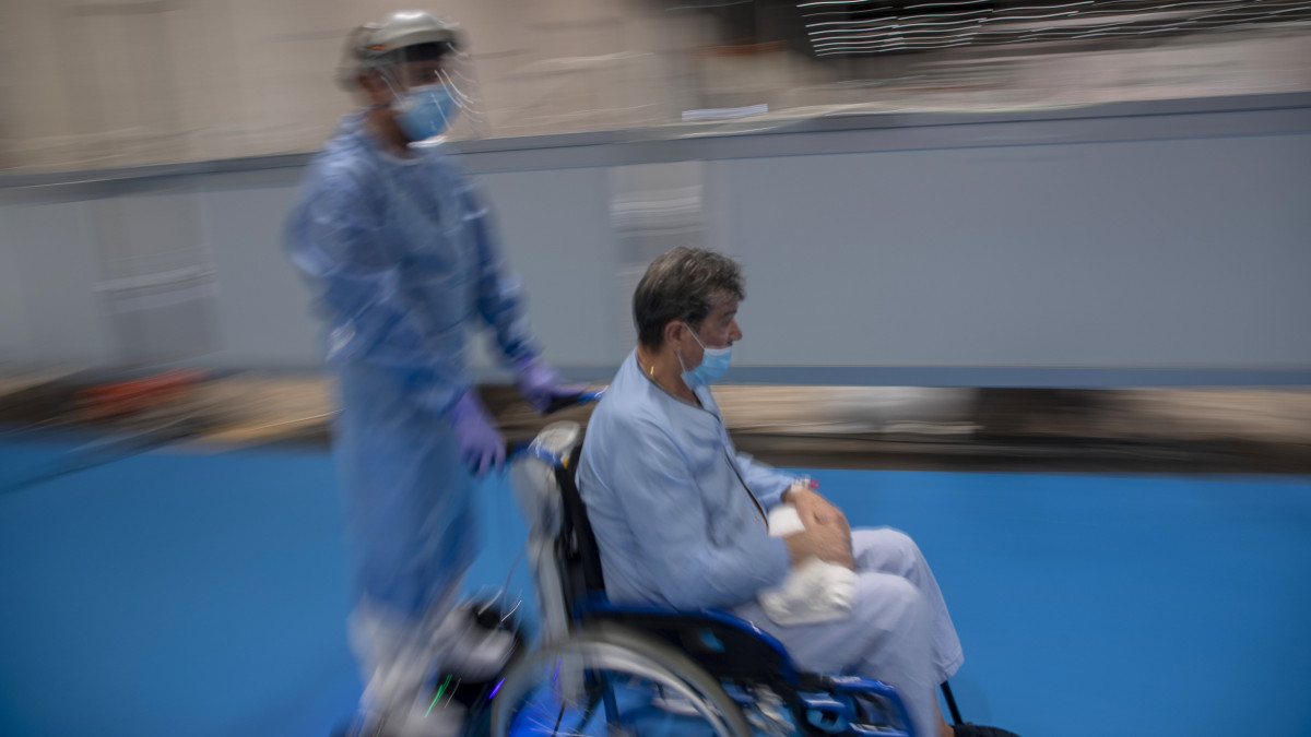 Kerekesszékben ülő pácienst tol egy ápoló a koronavírussal fertőzött betegeknek a madridi Ifema kongresszusi és kiállítási központban berendezett ideiglenes kórházban a koronavírus-járvány idején, 2020. április 23-án.