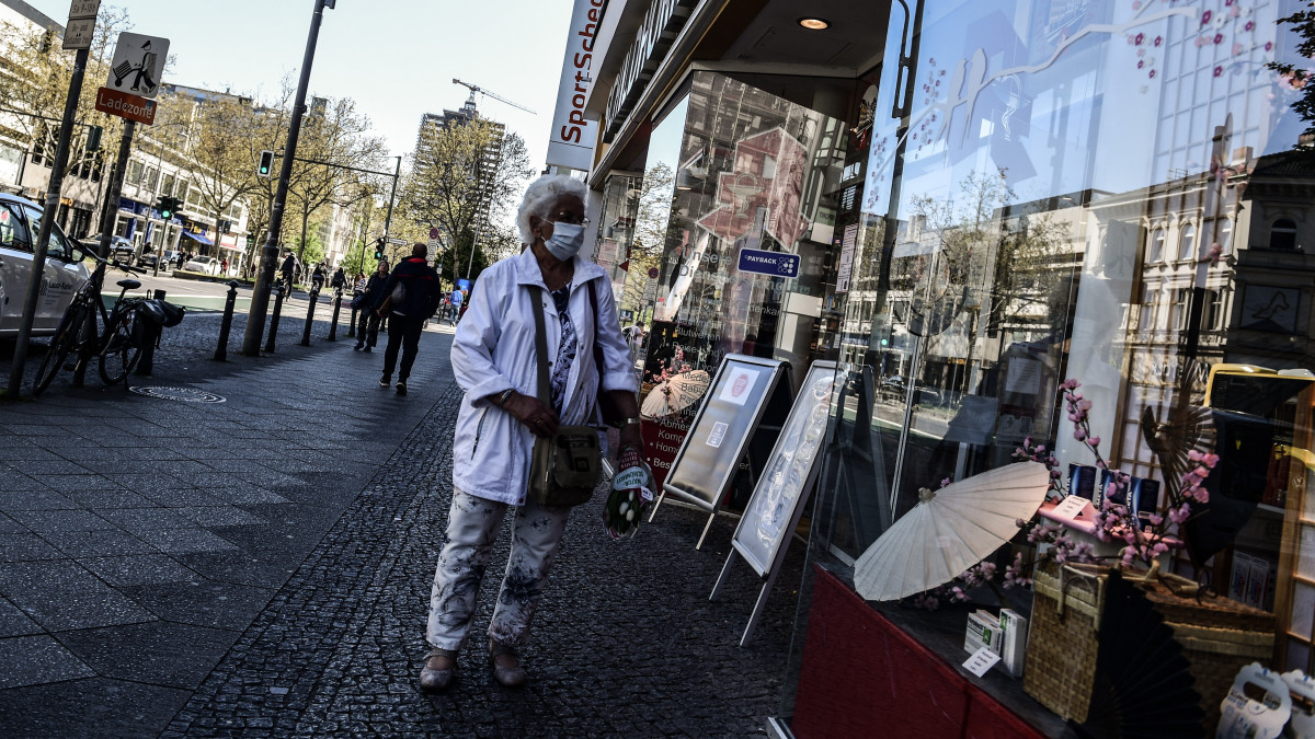 Járókelő egy kinyitott berlini üzlet kirakata előtt a koronavírus-járvány idején, 2020. április 22-én, amikor a német hatóságok engedélyezték a 800 négyzetméternél nem nagyobb eladótérrel rendelkező boltoknak a járvány miatti több hetes zárva tartás utáni újranyitást.