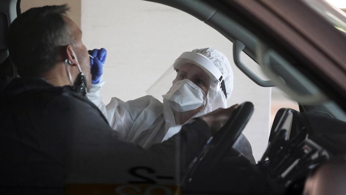 Védőruhát viselő egészségügyi dolgozó egy autóst tesztel egy varsói bevásárlóközpont parkolójában 2020. április 22-én, a koronavírus-járvány idején.