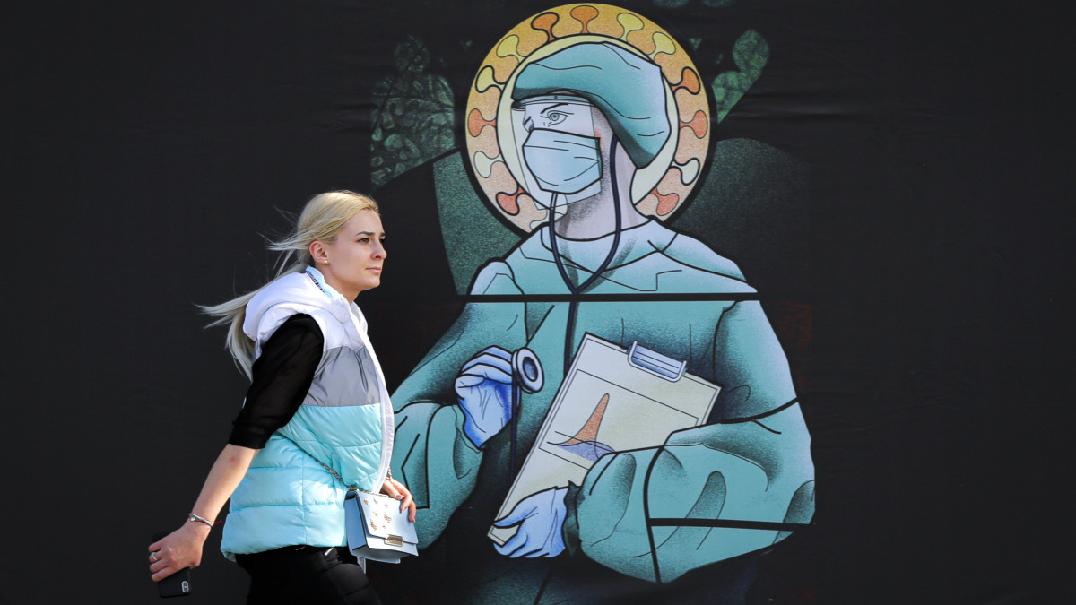 Védőmaszkot viselő egészségügyi dolgozó egy különböző vallások ikonográfiai elemeinek felhasználásával készült képen Bukarestben 2020. április 30-án. A Wanda Hutira tervező által készített kép egy kampány része, amelynek célja, hogy kifejezze az orvosok és ápolók munkája iránt érzett köszönetet. A román ortodox egyház istenkáromlásra hivatkozva elítélte a képsorozatot.
