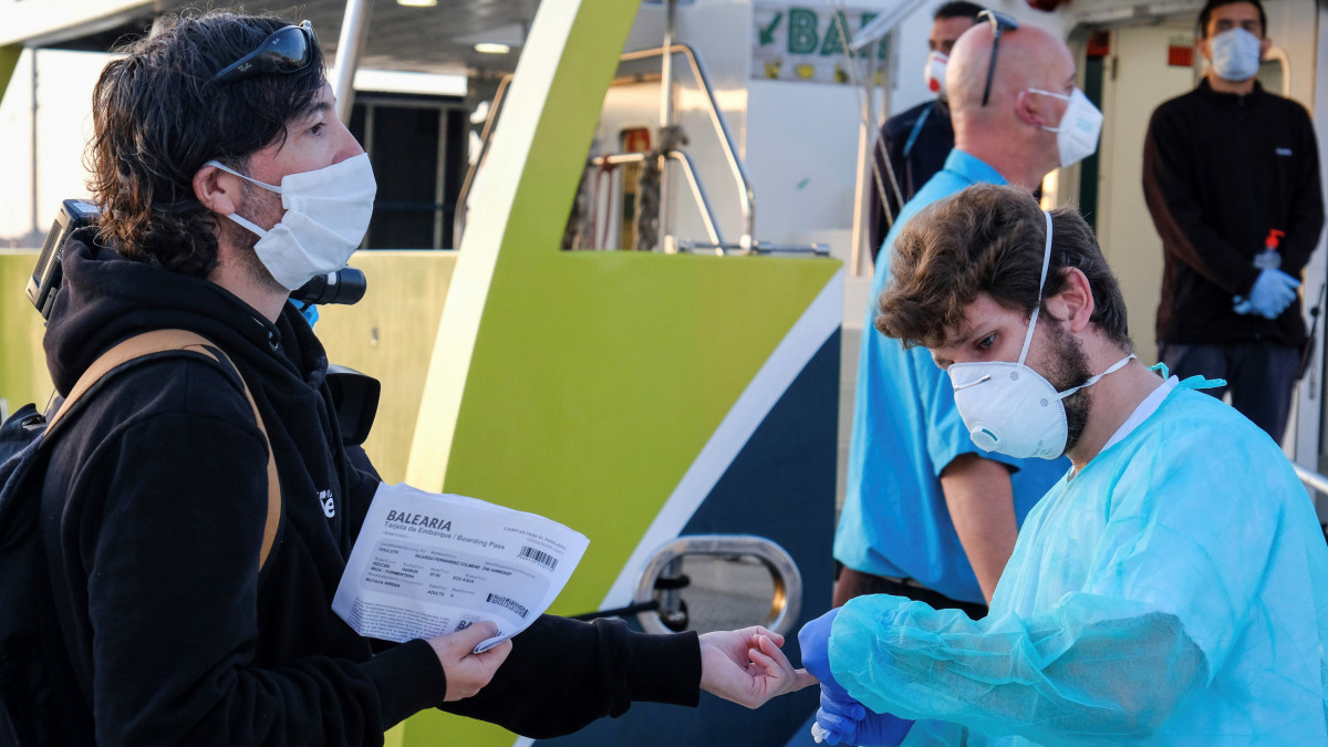 Védőmaszkot viselő egészségügyi dolgozó koronavírustesztet végez a spanyolországi Ibiza szigetéről induló komp egyik utasán, mielőtt felengednék őt a hajóra 2020. május 4-én. A spanyol kormány megkezdte a koronavírus-járvány miatt bevezetett kijárási korlátozások enyhítését.