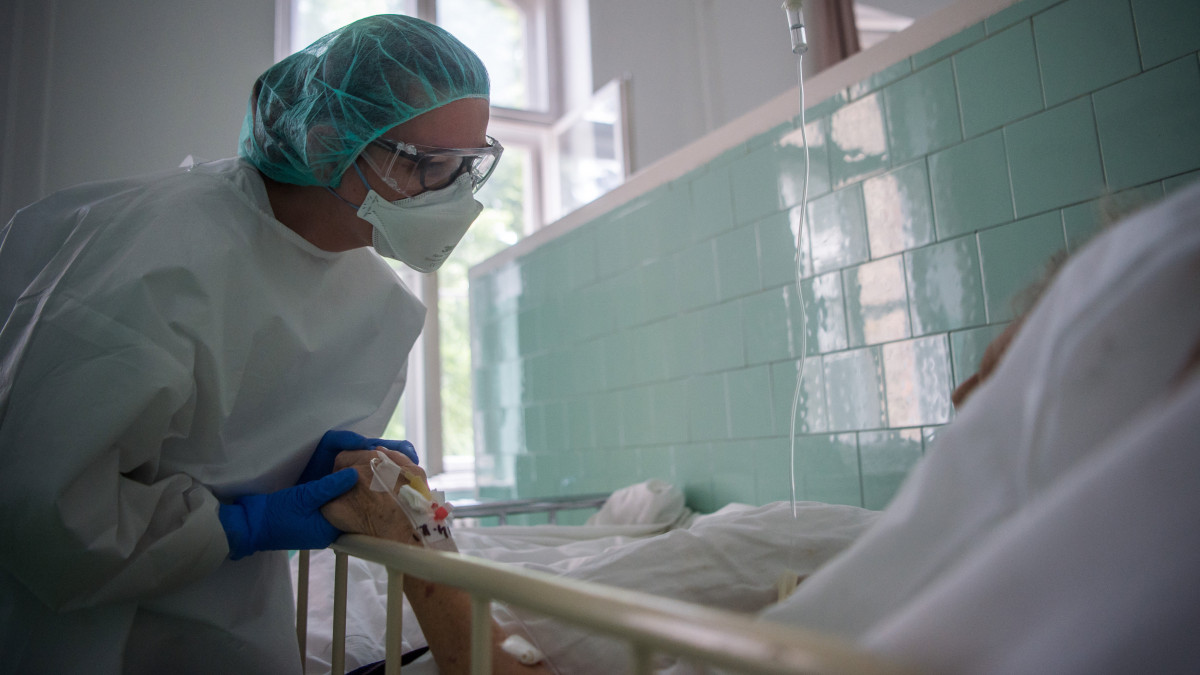 Védőfelszerelést viselő ápoló megsimogatja egy beteg kezét a koronavírussal fertőzött betegek fogadására kialakított Covid Ortopéd-Traumatológiai Osztályon a fővárosi Szent János Kórházban 2020. május 14-én.