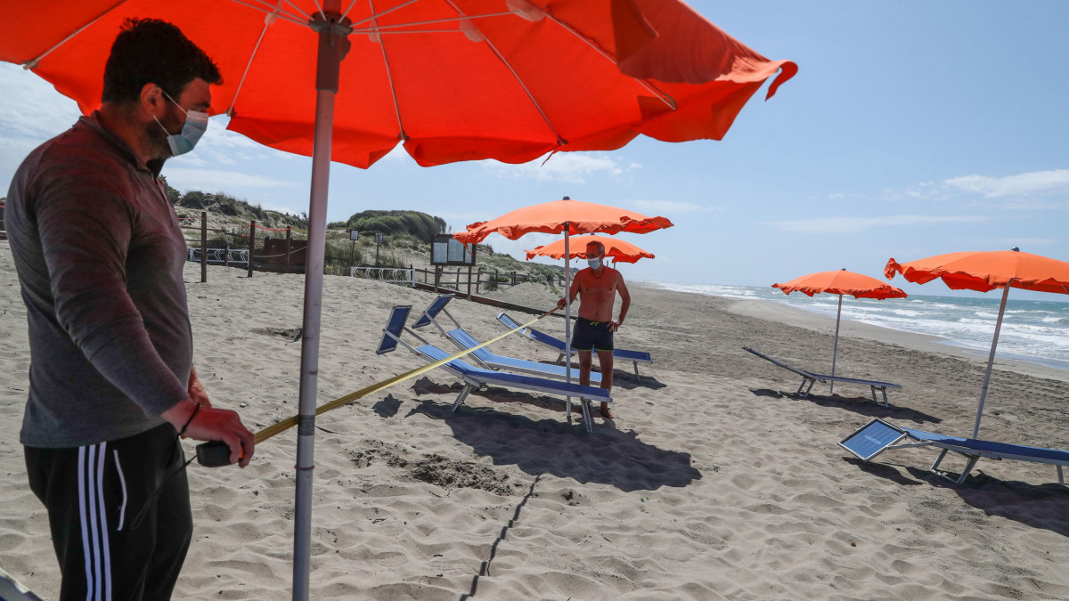A napozóágyak közötti biztonságos távolságot mérik munkások Capocotta tengerpartján 2020. május 12-én, a koronavírus-járvány elleni védekezés második szakaszában. Olaszországban a bevezetett óvintézkedéseket fokozatosan négy fázisban oldják fel, április 27-től négy egymást követő hétfőn újabb és újabb korlátozó intézkedéseken enyhítenek.