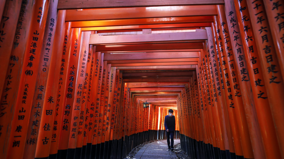 Védőmaszkos férfi megy sintó szentélykapuk, eredeti nevén torii-k között a kiotói Fusimi Inari-nagyszentélyben 2020. május 13-án. Abe Sindzó japán kormányfő május 31-ig hosszabbította meg a járvány miatt kihirdetett szükségállapotot a szigetországban.