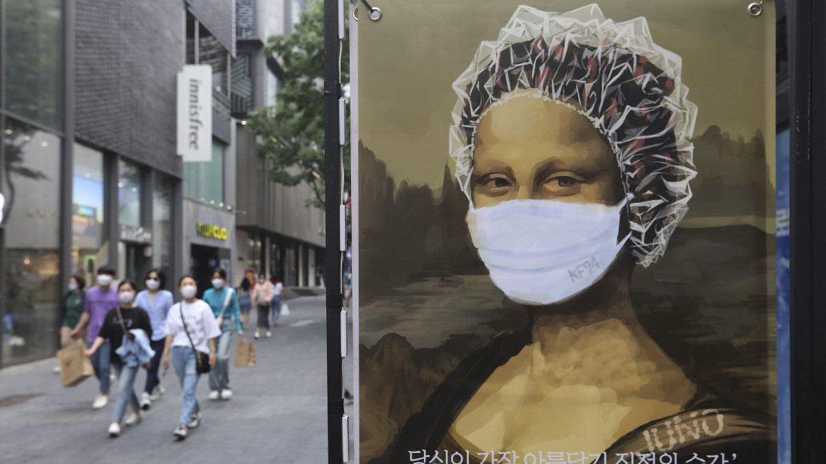 Szájmaszkot és hajvédő sapkát visel Leonardo da Vinci olasz reneszánsz művész Mona Lisájának mása egy fodrászüzlet cégtábláján Szöulban 2020. május 26-án, a koronavírus-járvány idején.