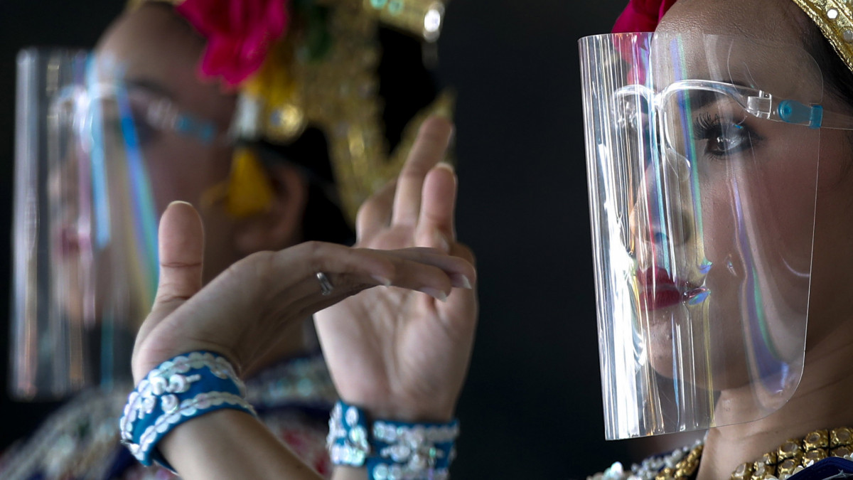 Arcvédő műanyag pajzsban lépnek fel thaiföldi táncosnők egy vallási ünnepségen a bangkoki Eravan szentélyben 2020. május 28-án. Thaiföldön június 30-ig meghosszabbítják a koronavírus-járvány miatt kihirdetett rendkívüli állapotot.