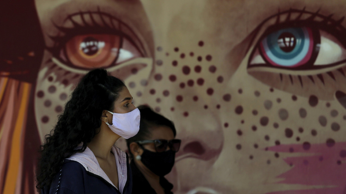 A koronavírus-járvány miatt védőmaszkot viselő nők sorban állnak egy iskola udvarán felállított ideiglenes koronavírus-tesztelő állomáson, egy falfestmény előtt Brazíliavárosban 2020. május 26-án.