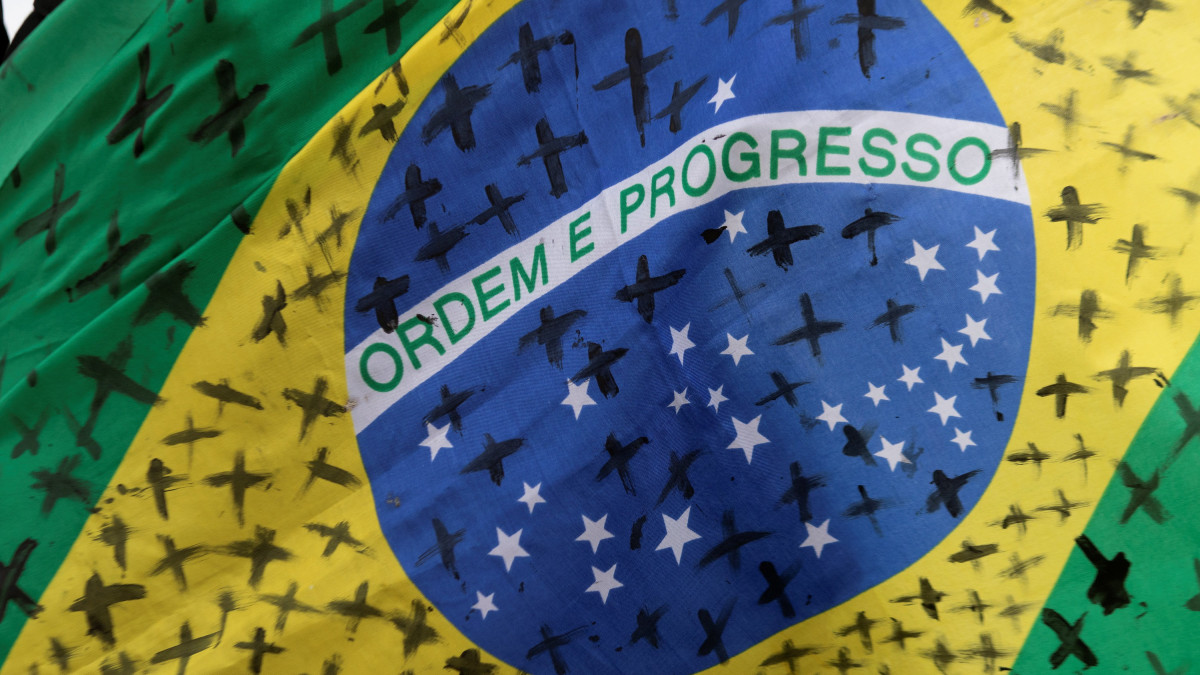Fekete kereszteket festettek a brazil zászlóra a koronavírus-járvány áldozatainak emlékére egy tüntetésen Brazíliavárosban 2020. május 20-án. A tüntetők Jair Bolsonaro brazil elnök koronavírus-járvánnyal kapcsolatos intézkedései ellen tiltakoztak. Előző nap Brazíliában először haladta meg az ezret az egy nap alatt elhunytak száma.