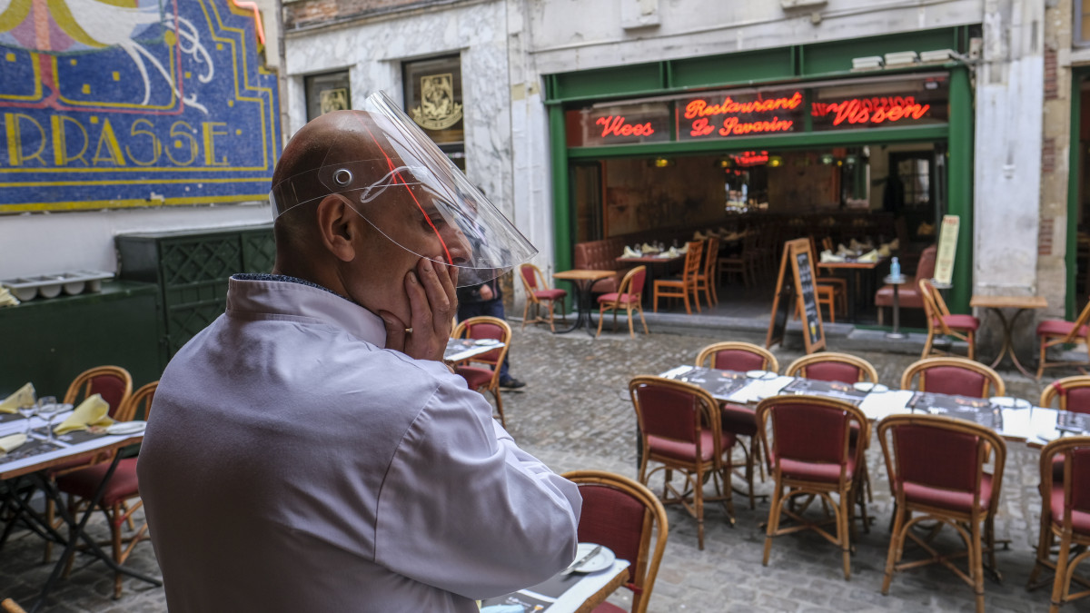 Arcpajzsot viselő pincér várja a vendégeket egy étterem teraszán Brüsszel belvárosában 2020. június 8-án. Az éttermek és kávézók tulajdonosainak beszámolója szerint kevés a vendég, mióta a koronavírus-járvány miatti korlátozások enyhítésének köszönhetően újra kinyitották a vendéglátóhelyeket.