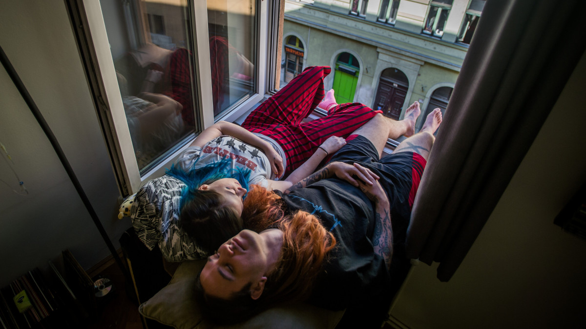 A koronavírus-járvány miatt önkéntes karanténban lévő zenész és sminkes párja pihen budapesti otthonuk ablakában 2020. április 6-án.