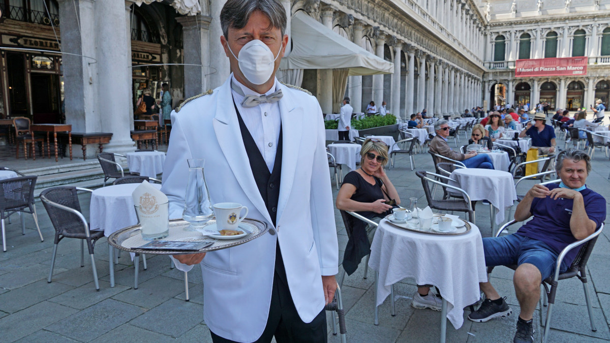 Védőmaszkot viselő pincér és vendégek a Caffe Florian teraszán, a velencei Szent Márk téren 2020. június 12-én, miután a koronavírus-járvány miatt három hónapos zárva tartást követően az egyik legrégebbi  olasz vendéglátóhely újranyitott.