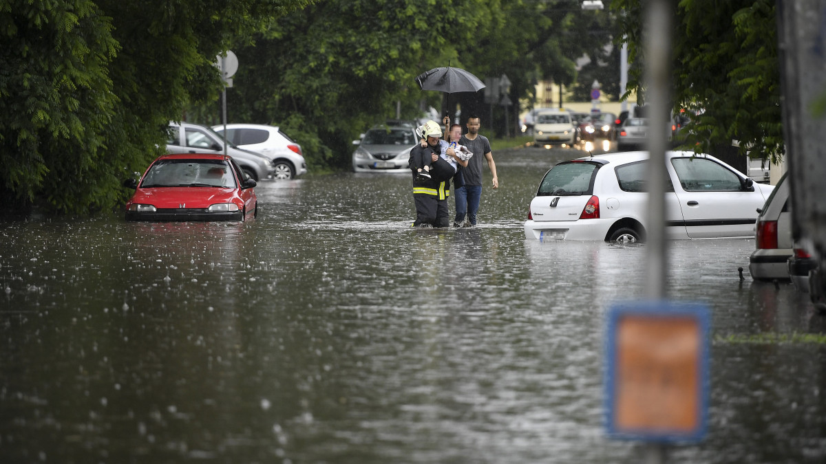 Elakadt autó utasát viszi karjaiban egy tűzoltó az esővízzel elöntött Salétrom utcában Debrecenben 2020. június 16-án.