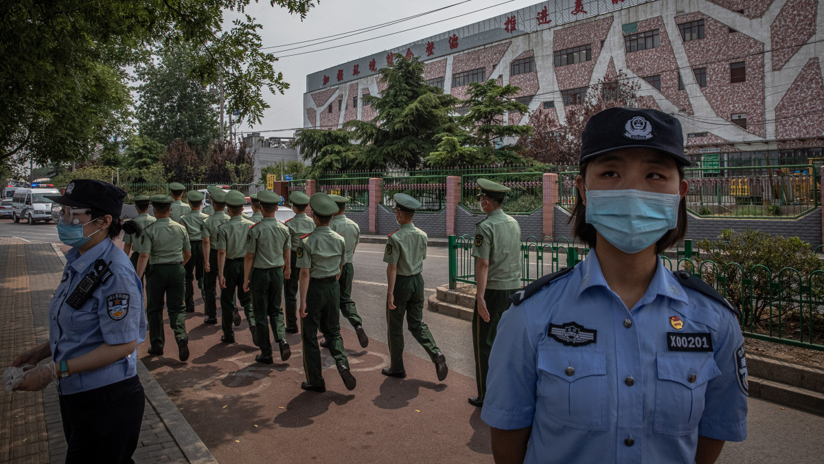 A koronavírus-járvány miatt védőmaszkot viselő rendőrök őrt állnak a pekingi Hszinfadi nevű nagybani piac épülete közelében 2020. június 13-án. A piacot lezárták, miután a hatóságok a helyben továbbadott koronavírusos esetek számának megugrását jelentették.