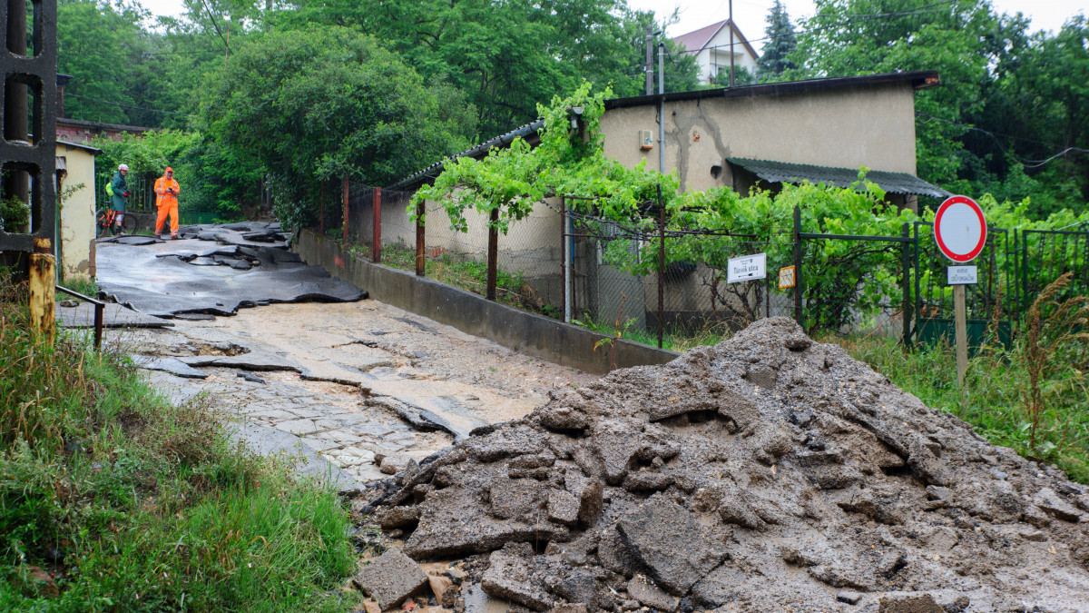 Sárral és aszfaltdarabokkal borított utca Pilisborosjenőn 2020. június 14-én. A Pest megyei községben a lezúduló esővíz egy mezőgazdasági területről a földet, valamint az útburkolatot elsodorva elöntötte és járhatatlanná tette a 10-es főút egy szakaszát.