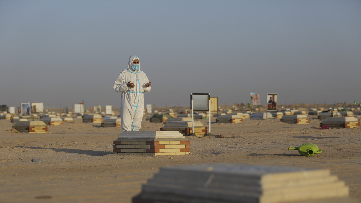 A 2020. július 24-én közreadott képen az Ali imám Brigádok egyik tagja imádkozik egy koronavírus-fertőzésben elhunyt ember sírja mellett az iraki Nedzsef egyik temetőjében július 20-án. Ezt a temetőt a koronavírus-járvány áldozatai számára alakították ki, miután az ország többi temetője nem vállalja a fertőzésben elhunyt emberek temetését.