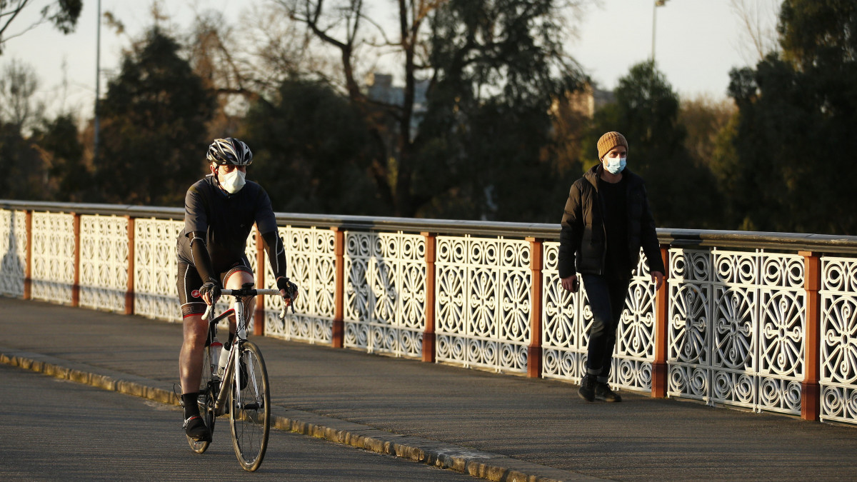 Védőmaszkot viselő ember kerékpározik a Yarra nevű folyó mentén a Victoria állambeli Melbourne-ben 2020. július 24-én. Az államban megnőtt az azonosított koronavírus-fertőzöttek száma, ezért július 22-től kötelezővé tették a maszk viselését. A szabály megszegéséért akár 200 dollár bírságot is kiszabhatnak.