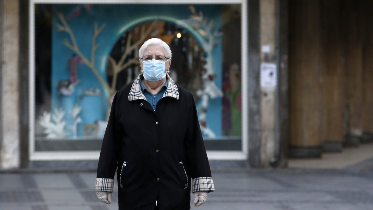 Védőmaszkot viselő idős nő áll egy belgrádi utcán 2020. április 21-én. Szerbiában ettől a naptól kezdve rövidítik a kijárási tilalom óráit, a március közepe óta szobafogságra ítélt nyugdíjasok heti háromszor rövid sétát tehetnek a lakhelyük környékén, és fokozatosan kinyithatnak a műhelyek, edzőtermek, fodrász- és kozmetikai szalonok, május közepétől pedig a szállodák és a vendéglátóhelyek is.