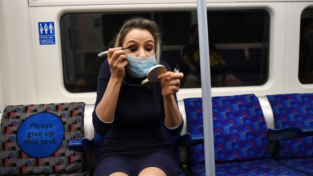 Védőmaszkos nő sminkeli magát a londoni metrón munkába menet 2020. augusztus 4-én. Míg a kormány arra ösztönzi a briteket, hogy használják a tömegközlekedést és térjenek vissza munkahelyükre, egy friss felmérés szerint a koronavírus-járvány miatt a dolgozók 45 százaléka továbbra is otthonról dolgozik.