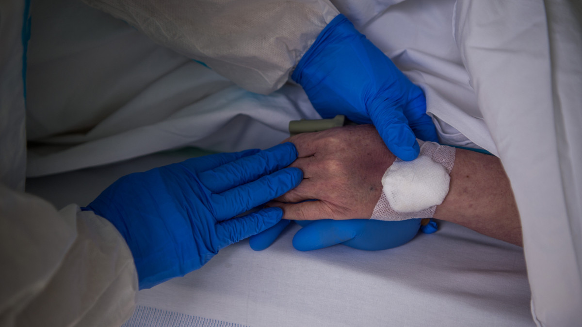 Védőfelszerelést viselő ápoló megsimogatja egy beteg kezét a koronavírussal fertőzött betegek fogadására kialakított intenzív osztályon az Országos Korányi Pulmonológiai Intézetben 2020. május 5-én.