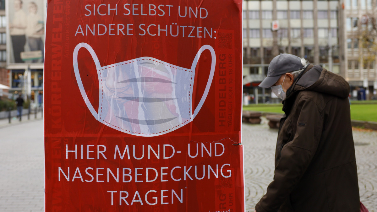 Védőmaszkos járókelő a németországi Mannheimban 2020. október 30-án. A koronavírus-járvány miatt a baden-württembergi tartományi kormány szigorította a korlátozó intézkedéseket. A plakát a maszkviselés kötelező voltára hívja fel a figyelmet.