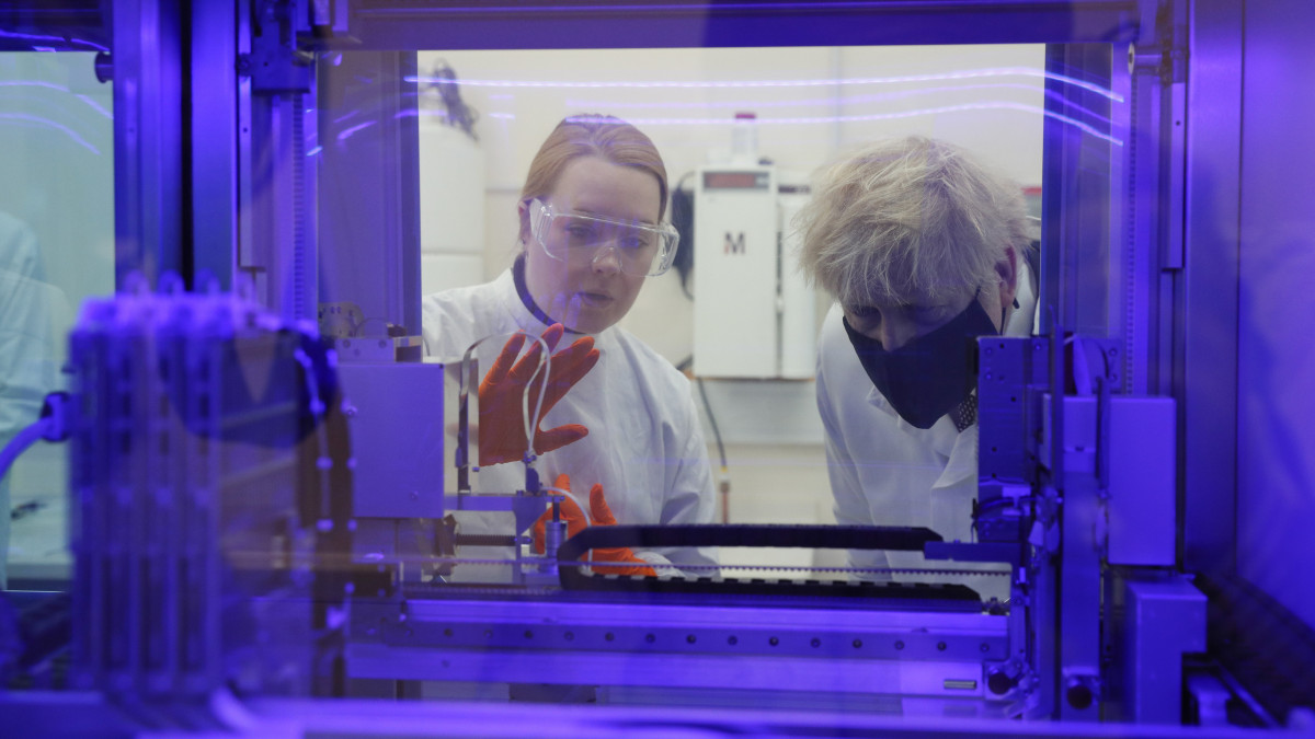 A koronavírus-járvány miatt védőmaszkot viselő Boris Johnson brit miniszterelnök egy PCR diagnosztikai műszert néz a brit közegészségügyi kormányhivatal egyik laboratóriumában tett látogatása során az angliai Salisbury közelében fekvő Porton Down technológiai központban 2020. november 27-én.