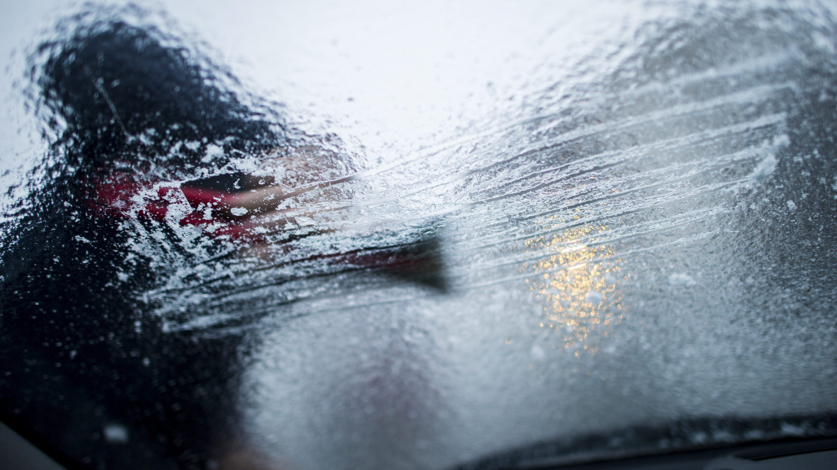 Egy férfi kaparja az autója szélvédőjéről a ráfagyott ónos esőt Pécsen 2016. január 6-án.