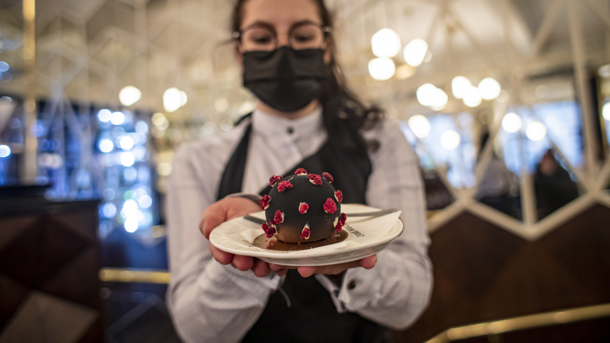 Védőmaszkot viselő alkalmazott egy koronavírushoz hasonlító süteményt szolgál fel egy prágai cukrászdában 2020. december 3-án. Csehországban ettől a naptól kezdve újra kinyithattak a koronavírus-járvány miatt október 14. óta zárva tartó éttermek és kávézók.