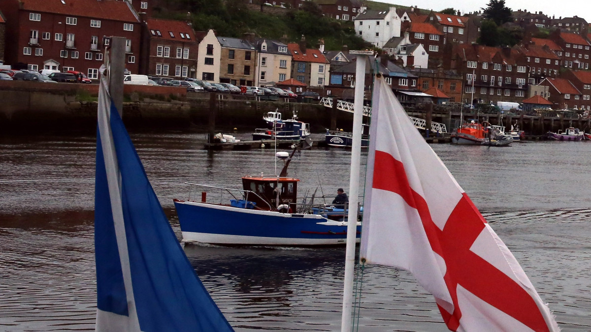 Whitby, 2016. június 21.Halászhajó fut ki az észak-angliai Whitby kikötőjéből, az előtérben egy angol zászló (j) 2016. június 15-én, nyolc nappal a brit EU-tagságról rendezett népszavazás előtt. A brit halászati ipar erősen kilépéspárti. (MTI/EPA/Nigel Roddis)
